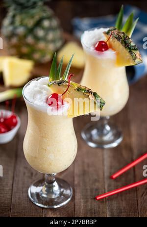 Cocktail Pina colada garni de cerise, de tranches d'ananas et de feuilles sur une table rustique en bois Banque D'Images