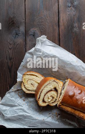 Gâteau à la cannelle cuit dans un moule à pain et servi entier et coupé en tranches avec du papier de cuisson isolé sur fond de table en bois sombre. Plan de travail avec espace de copie Banque D'Images
