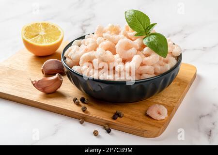 Crevettes Frosen dans un bol préparé pour la cuisson. Sur une planche à découper, bouillie les queues de crevettes pelées, le citron, l'ail et le poivre. Concept de recette de fruits de mer. Banque D'Images