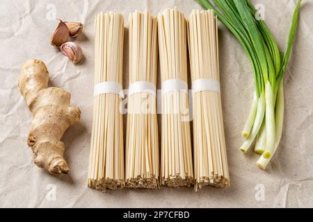 Des paquets de nouilles udon crues et d'épices en gros plan. Pains de pâtes végétaliennes japonaises séchées à base de farine de blé, de scallion, de gingembre et d'ail sur papier émietté Banque D'Images