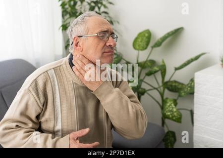 Homme âgé ayant mal de dents touchant la joue souffrant de douleurs assis sur un canapé à la maison. Banque D'Images