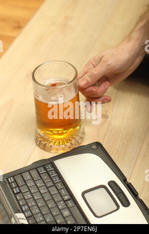 personne tenant une tasse à bière à côté d'un ancien ordinateur portable Banque D'Images