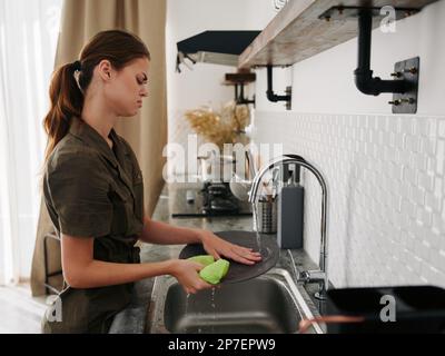 Femme fatiguée et irritée mains sans gants lave la vaisselle avec une éponge de lavage de vaisselle avec des bulles, des tâches ménagères, un look insatisfait, pas de lave-vaisselle Banque D'Images