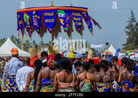 Procession des adeptes d'un temple voodoo sous leur bannière parapluie au terrain de parade de plage à Ouidah au festival voodoo annuel Banque D'Images