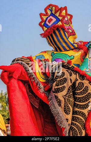 l'eguinguin aux couleurs vives avec masque à rayures pointe une main gantée rouge vers l'extérieur lors du festival voodoo annuel de ouidah au bénin Banque D'Images