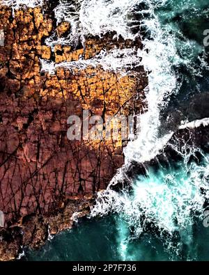 Une scène tranquille de vagues s'écrasant contre des rochers près de la rive, illuminée par le soleil et mise en évidence par de petites casquettes blanches Banque D'Images