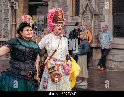 Deux femmes de steampunks sourient alors qu'elles marchent dans une procession de rue. Ils portent des vêtements de style victorien et l'une des femmes a un étui de tasse de thé. Banque D'Images