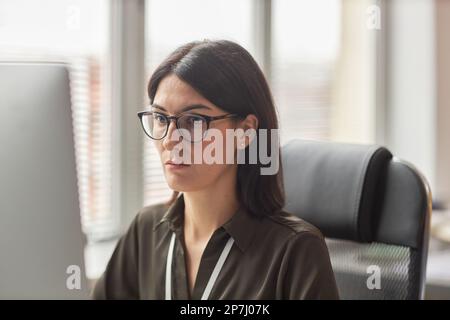 Portrait d'une femme d'affaires ciblée portant des lunettes en utilisant un ordinateur sur le lieu de travail Banque D'Images