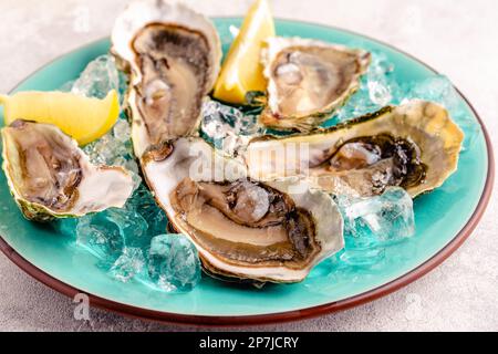 Huîtres fraîches ouvertes sur une assiette bleue, servies avec du citron et de la glace. Banque D'Images