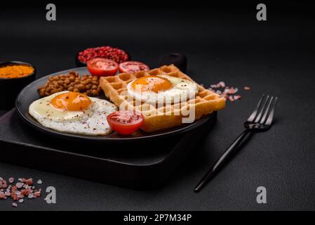 Délicieux petit déjeuner copieux composé d'un œuf frit, de gaufres belges, de lentilles, de microverts aux épices et aux herbes sur fond de béton sombre Banque D'Images