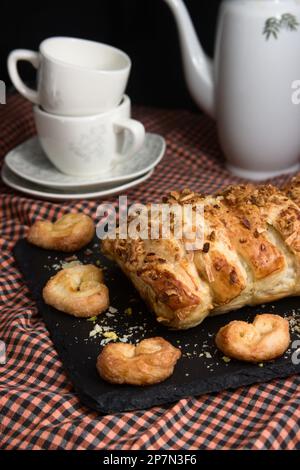 Image d'une pâte feuilletée remplie de chocolat à côté de quelques tasses traditionnelles et d'une cafetière sur une table. En-cas sucré maison Banque D'Images