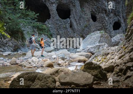 Un couple de randonneurs sautant sur les rochers tout en traversant la rivière de montagne, en passant par une visite à pied dans la gorge. Concept de mode de vie voyage et aventure. Banque D'Images