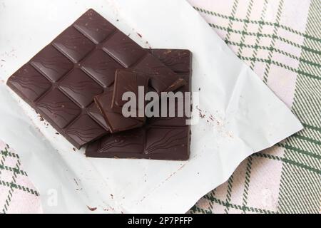 Gros plan d'une barre de chocolat noir hachée sur le papier qui l'enveloppe sur une nappe rayée Banque D'Images