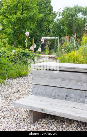 Un banc en bois vous invite à vous attarder dans le petit jardin potager sauvage sur l'ancien parc industriel surcultivé de Hambourg. Le sol est de Banque D'Images