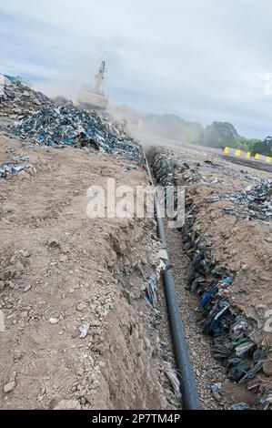 Un tuyau perforé pour le méthane est déposé dans une tranchée qui sera enfouie dans une décharge active. Banque D'Images