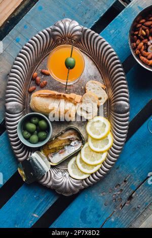 plateau à snacks en conserves de sardines au poisson plateau argenté avec amandes, pain, olives vertes, tranches de citron et cocktail d'orange Banque D'Images