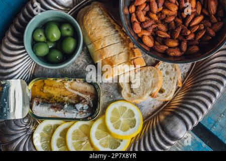 vue en grand angle de la boîte de poisson sardines plateau d'en-cas argent avec amandes, pain, olives vertes, tranches de citron sur palette en bois Banque D'Images