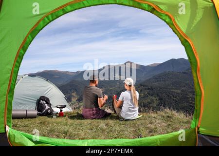 Couple avec des boissons appréciant le paysage de montagne, vue de la tente de camping Banque D'Images