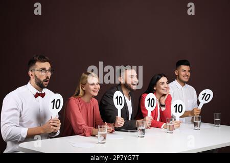 Panel de juges portant des affiches avec le score le plus élevé à la table sur fond marron Banque D'Images