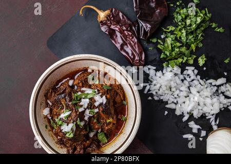 Un bol de viande de bœuf bigria cuite lentement et braisée dans un bol d'époque avec des oignons hachés, de la coriandre, des poivrons guajillo et du bouillon Banque D'Images