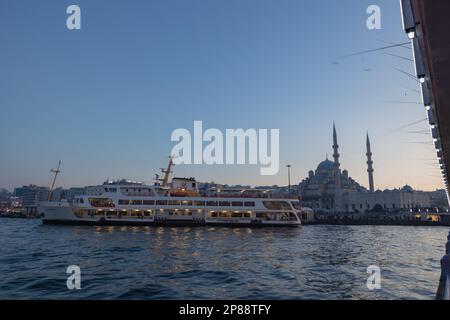 Photo d'Istanbul. Ferry et Yeni Cami aka Nouvelle mosquée dans le quartier d'Eminonu au coucher du soleil depuis le pont de Galata. Istanbul Turkiye - 12.24.2022 Banque D'Images