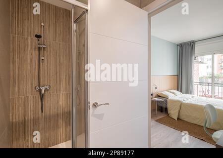 Vue de la petite salle de bains avec douche sur la chambre double avec une fenêtre donnant sur le balcon et la cour. Concept d'un hôtel respectable Banque D'Images