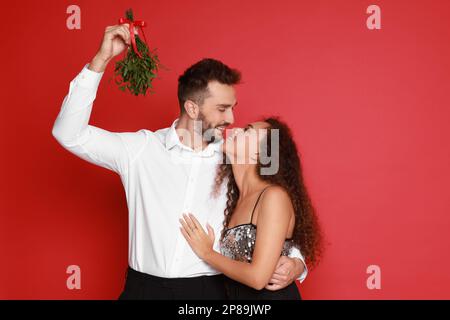 Un couple charmant sous un bouquet de GUI sur fond rouge Banque D'Images