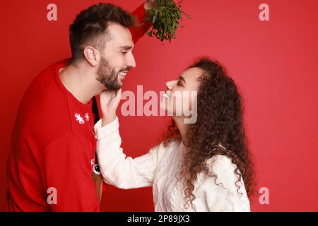 Un couple charmant sous un bouquet de GUI sur fond rouge Banque D'Images