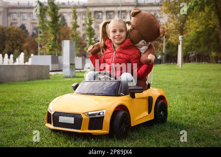 Petite fille mignonne jouant avec un ours en peluche et une voiture pour enfants dans le parking Banque D'Images