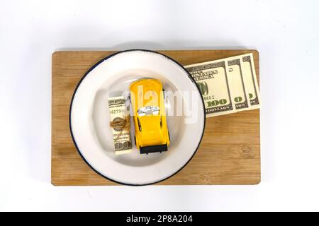 Modèle de voiture jaune miniature sur fond de facture de billets en dollars américains. Plan d'affaires, de finances ou de budget économiser de l'argent pour l'achat d'une nouvelle voiture et l'assurance auto Banque D'Images