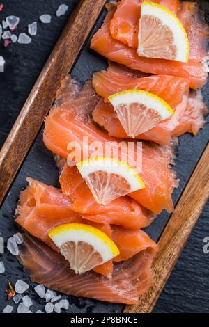 Filets de saumon frais crus. Carpaccio de saumon servi avec du sel et du citron sur une planche à découper noire. Banque D'Images