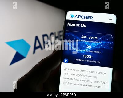 Personne tenant un téléphone portable avec une page Web du logiciel de gestion des risques Archer (RSA Security) à l'écran avec logo. Concentrez-vous sur le centre de l'écran du téléphone. Banque D'Images