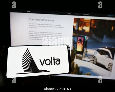 Personne tenant un téléphone portable avec le logo de la compagnie d'infrastructure EV Volta Charging LLC sur l'écran devant la page Web d'affaires. Mise au point sur l'affichage du téléphone. Banque D'Images