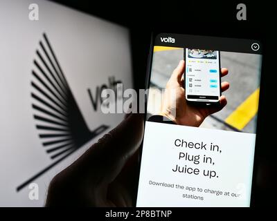 Personne tenant le téléphone portable avec la page web de la compagnie d'infrastructure EV Volta Charging LLC à l'écran avec le logo. Concentrez-vous sur le centre de l'écran du téléphone. Banque D'Images