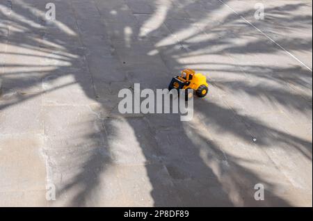 Rue avec carreaux de pierre. Jouet jaune oublié pour enfants - tracteur à l'ombre d'un palmier. Casillas del Angel, Fuerteventura, Îles Canaries, Espagne. Banque D'Images