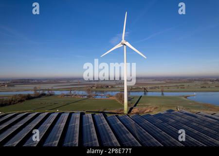 Panneaux solaires gelés devant l'éolienne solitaires, partie de l'industrie durable dans le paysage néerlandais de rivière plate contre le ciel bleu. Banque D'Images