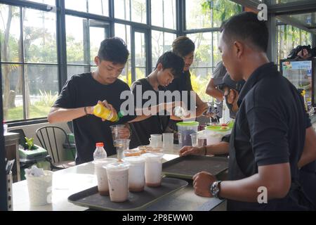 Le barman d'un café verse du lait et de la sauce tandis que le serveur attend devant lui Banque D'Images