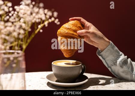 Gros plan d'une femme en train de tremper un croissant dans une tasse de café Banque D'Images