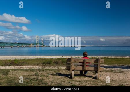Un long pont suspendu avec un homme assis sur un banc de parc en premier plan. Banque D'Images
