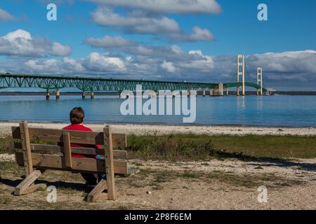 Un long pont suspendu avec un homme assis sur un banc de parc en premier plan. Banque D'Images