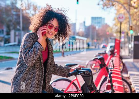 Femme parlant avec mobile tout en utilisant le système de vélo public Banque D'Images