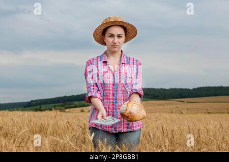 Jeune agriculteur détenant des dollars et du pain dans le champ de blé doré. Profitez de l'agriculture pendant la saison de récolte en été. Banque D'Images