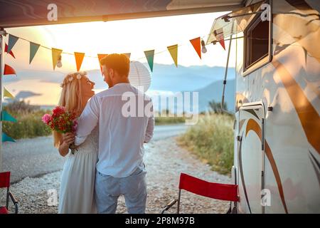 jeune couple caucasien adulte qui se embrasse, regardant l'un l'autre devant un campeur, à l'extérieur au coucher du soleil et belle vue Banque D'Images