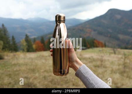 Femme tenant des thermos dorés dans les montagnes, gros plan Banque D'Images