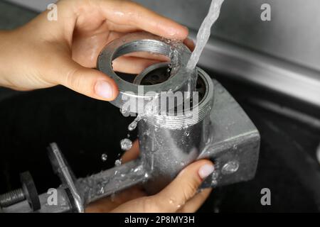 Femme lavant le moulin à viande manuel sous l'eau du robinet dans l'évier de cuisine à l'intérieur, gros plan Banque D'Images