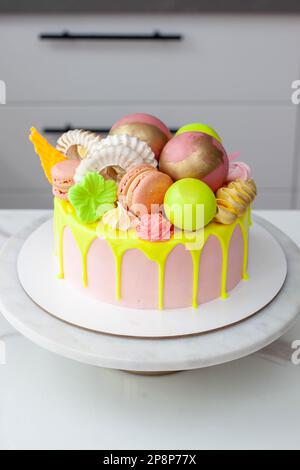 Gâteau d'anniversaire vert néons, citron vert et rose au goutte d'eau heureux surmonté d'un assortiment de fleurs en chocolat de couleur arc-en-ciel, de boules, de meringues et de bonbons Banque D'Images