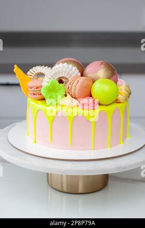 Gâteau d'anniversaire vert néons, citron vert et rose au goutte d'eau heureux surmonté d'un assortiment de fleurs en chocolat de couleur arc-en-ciel, de boules, de meringues et de bonbons Banque D'Images