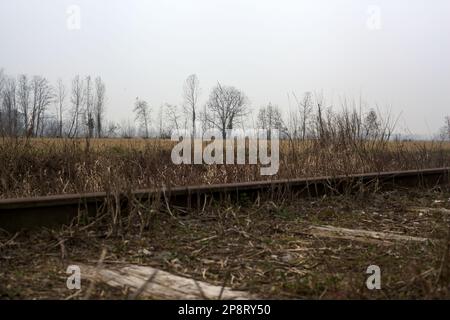 Voie de chemin de fer abandonnée à côté d'un champ cultivé dans la campagne italienne en hiver Banque D'Images