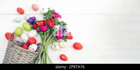 Fleurs de pavot et œufs de Pâques dans un panier en osier, fond de table en bois blanc, espace de copie. Banque D'Images