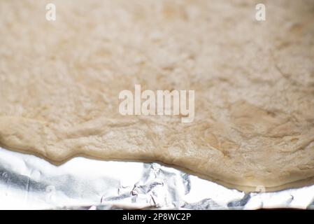 Pâte crue enroulée sur une plaque de cuisson. Base pour tarte ou pizza. Un morceau de pâte inégal à la maison Banque D'Images